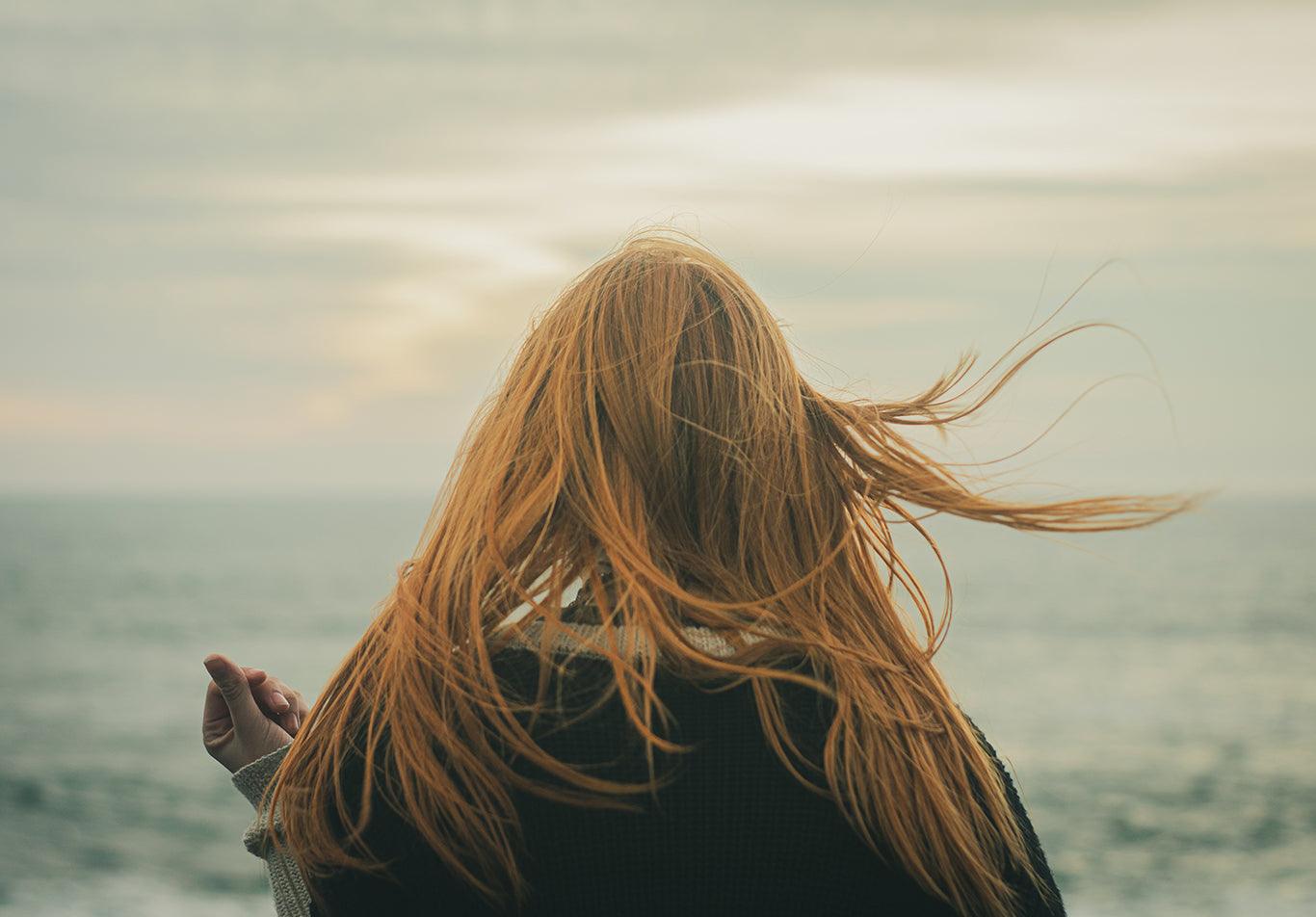 Una ragazza di spalle davanti al mare con i capelli fluenti